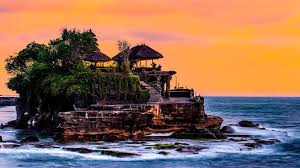 Tanah Lot Temple standing majestically on a rocky island surrounded by ocean waves at sunset.