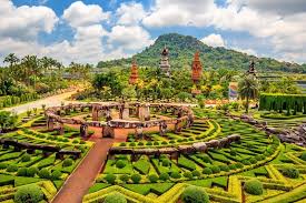 Ornate garden landscape at Nong Nooch Botanical Garden with trimmed hedges, colorful flowers, and traditional Thai architecture.