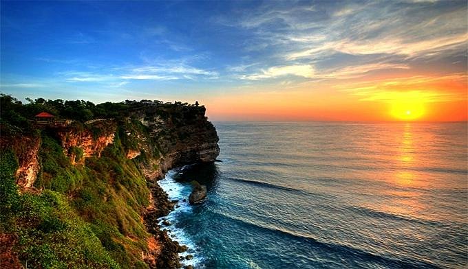 Uluwatu Temple perched atop a towering cliff with panoramic ocean views at sunset.