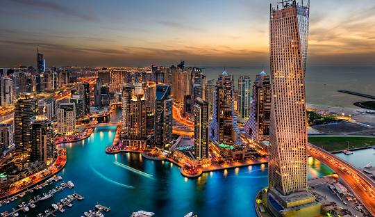 Dubai Marina skyline at sunset with illuminated buildings and water canal