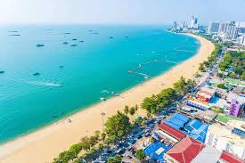 Bustling Pattaya Beach with people sunbathing, speedboats on the water, and the city skyline in the background.